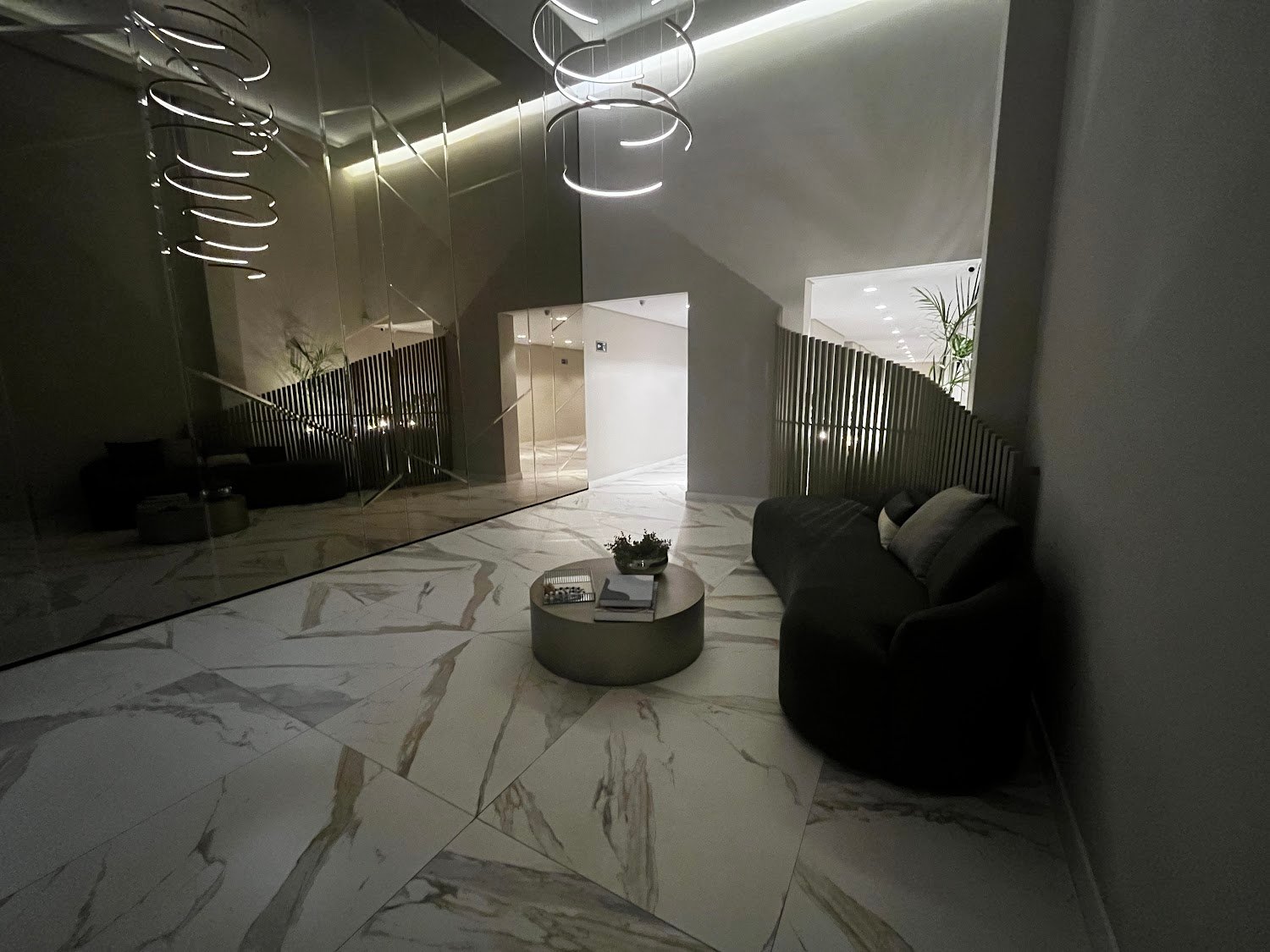 Foto real do lobby do Living Heredità Alto do Ipiranga, com piso de mármore e luminária de anéis